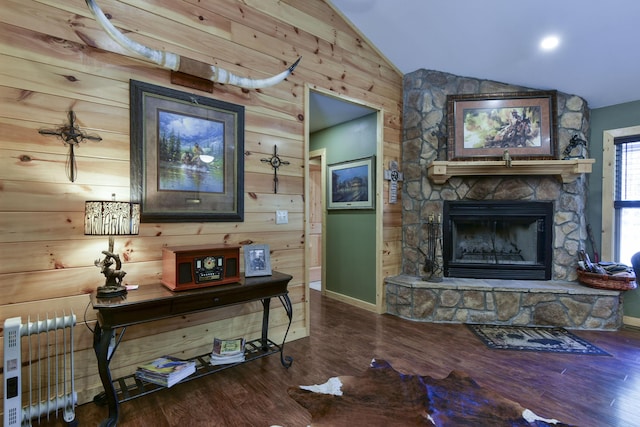 living room featuring baseboards, lofted ceiling, wood finished floors, a stone fireplace, and wood walls