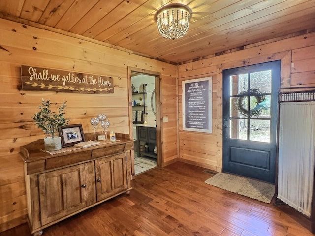 entryway with a chandelier, wooden ceiling, wood walls, visible vents, and dark wood finished floors