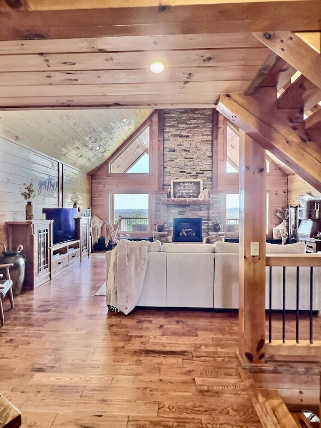 living area with wooden ceiling, wood walls, wood-type flooring, and a stone fireplace