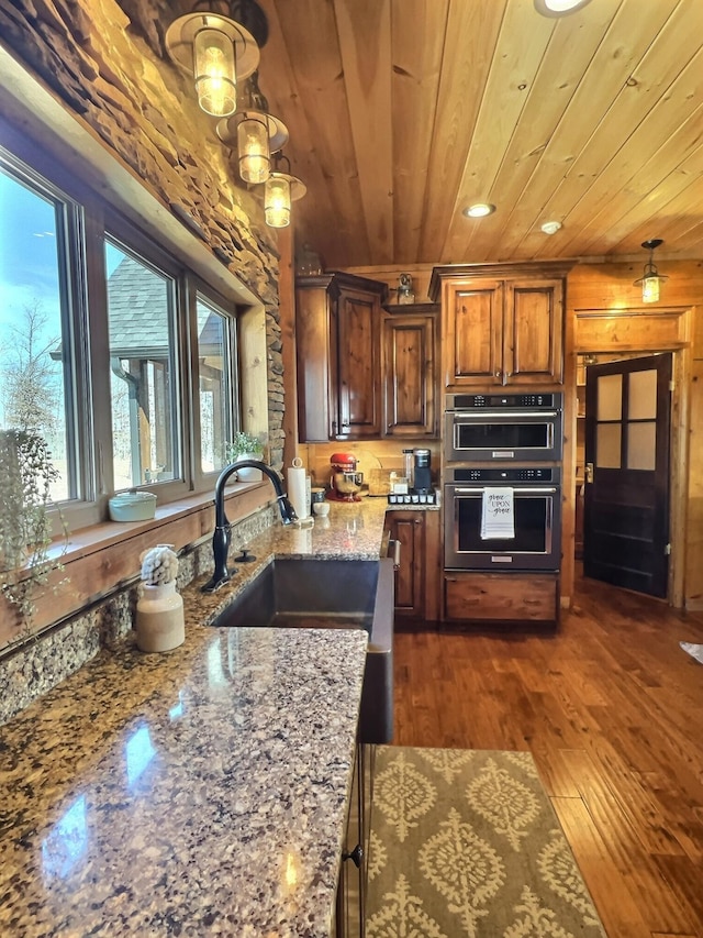 kitchen featuring wooden ceiling, dark wood-style floors, light stone countertops, multiple ovens, and a sink