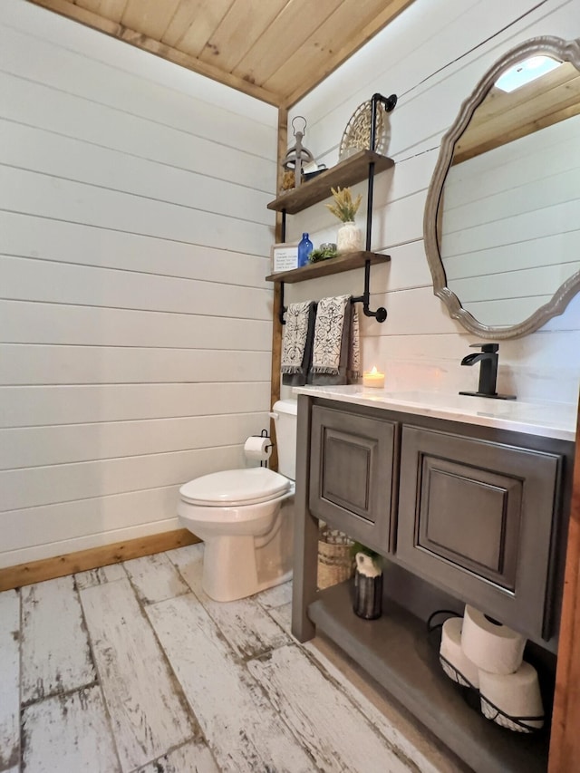 half bathroom featuring toilet, wood walls, wood ceiling, and vanity