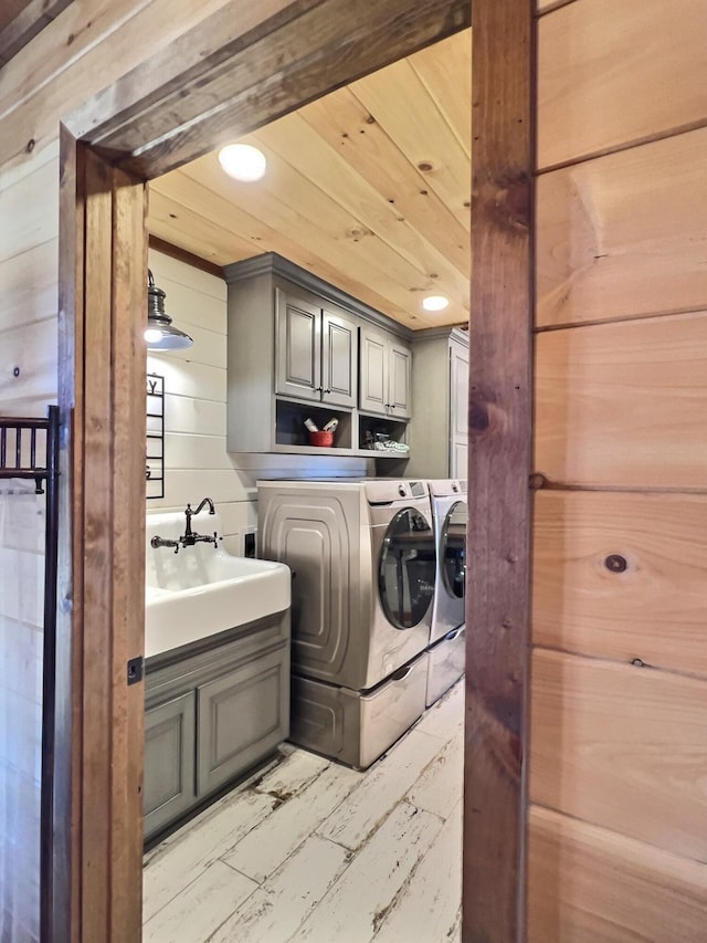 clothes washing area with cabinet space, washer and clothes dryer, wood ceiling, wood walls, and a sink