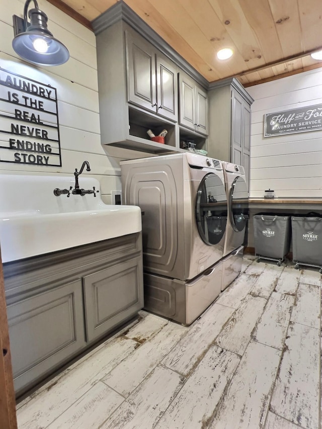 clothes washing area featuring cabinet space, wooden walls, washer and clothes dryer, wood ceiling, and a sink