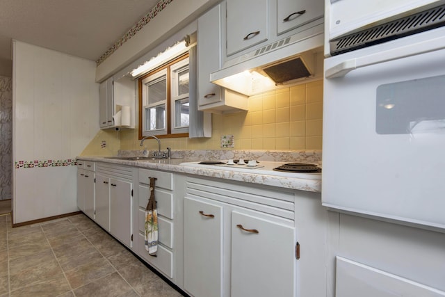 kitchen featuring light countertops, decorative backsplash, a sink, white appliances, and under cabinet range hood