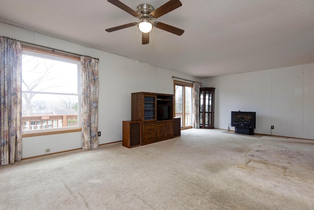 unfurnished living room with a ceiling fan, a wood stove, carpet flooring, and a textured ceiling