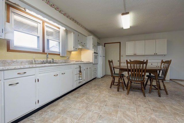 kitchen featuring white appliances, white cabinetry, a textured ceiling, and decorative backsplash