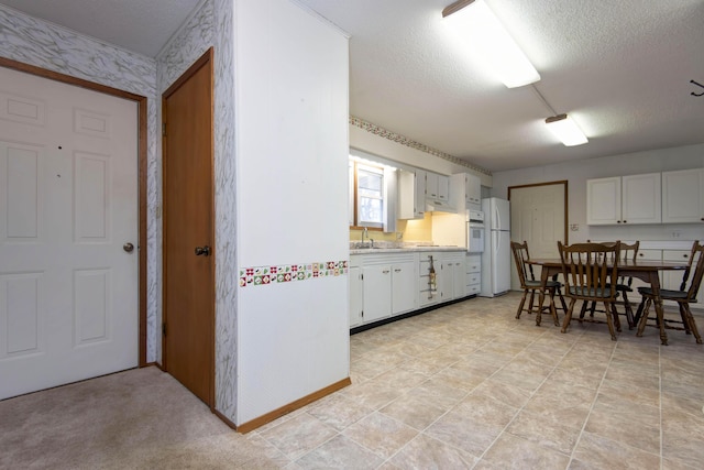 kitchen featuring white appliances, white cabinets, light countertops, a textured ceiling, and a sink