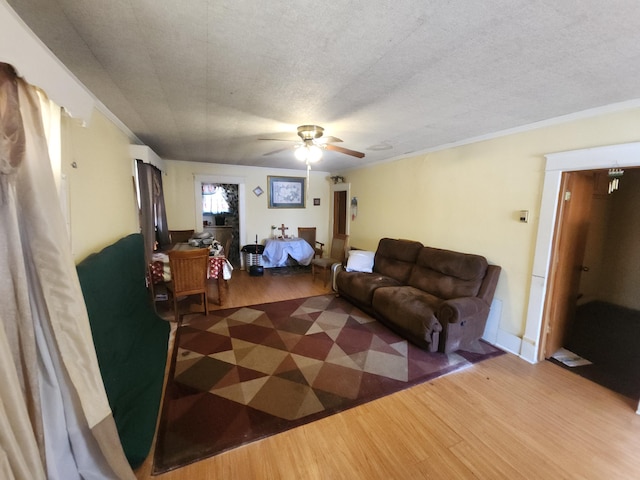 living room featuring a ceiling fan, crown molding, a textured ceiling, and wood finished floors