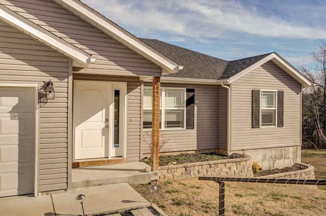 doorway to property with a garage and a shingled roof