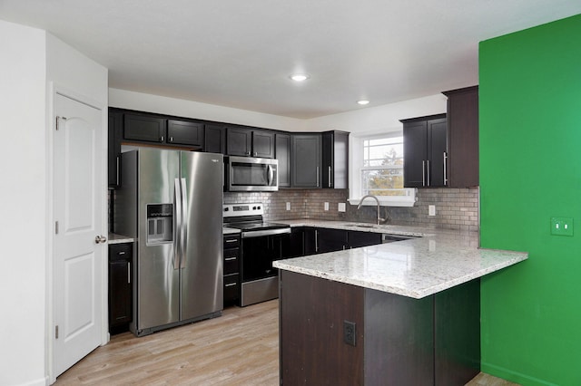 kitchen featuring a peninsula, appliances with stainless steel finishes, backsplash, light stone countertops, and light wood finished floors