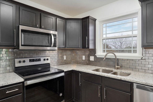 kitchen featuring light stone countertops, tasteful backsplash, stainless steel appliances, and a sink