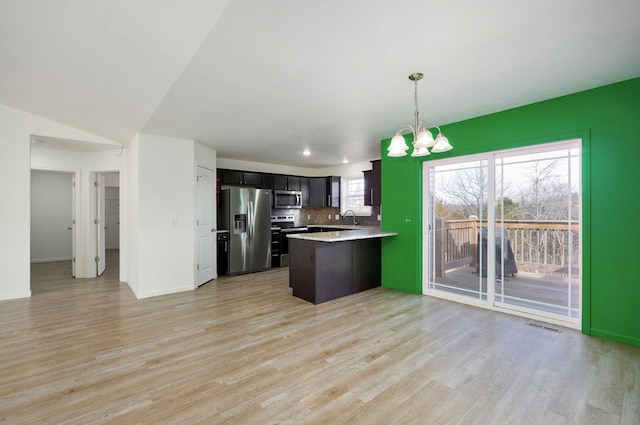 kitchen with stainless steel appliances, light countertops, light wood-style floors, a sink, and a peninsula