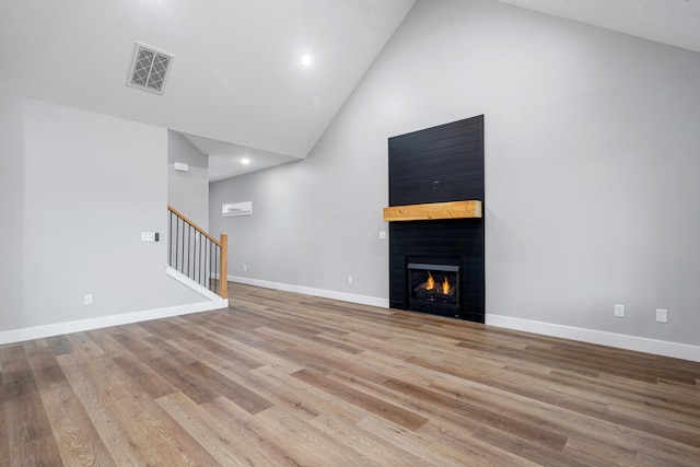 unfurnished living room with visible vents, light wood-style flooring, stairway, high vaulted ceiling, and a warm lit fireplace