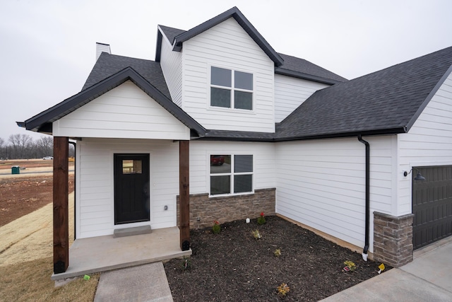 view of front facade featuring a garage, stone siding, a chimney, and roof with shingles