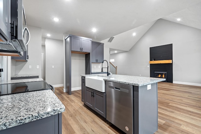 kitchen with a warm lit fireplace, light stone counters, a sink, light wood-style floors, and appliances with stainless steel finishes