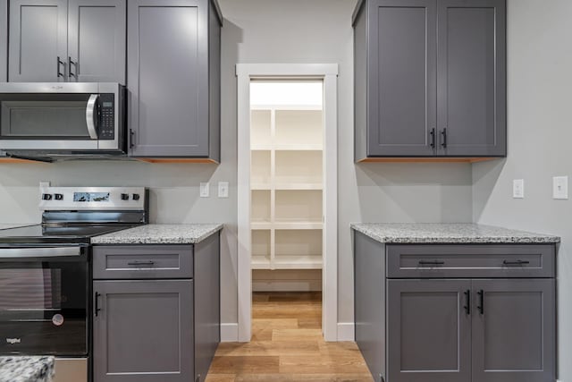 kitchen with light wood-style floors, appliances with stainless steel finishes, gray cabinets, and light stone counters