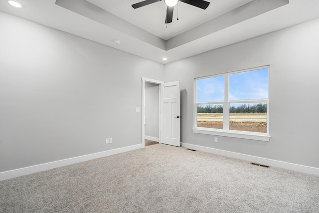 empty room featuring a tray ceiling, carpet, visible vents, and baseboards