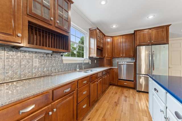 kitchen with light wood finished floors, appliances with stainless steel finishes, a sink, crown molding, and backsplash