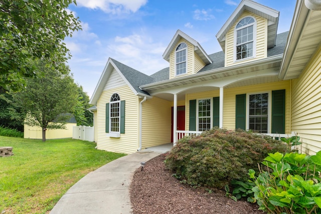 view of front facade with covered porch, a shingled roof, a front yard, and fence