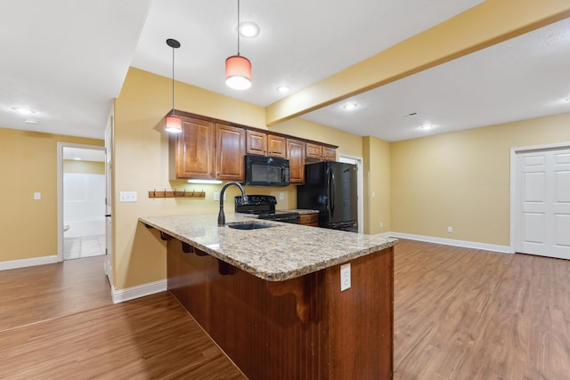 kitchen featuring a peninsula, a breakfast bar, baseboards, black appliances, and light wood finished floors