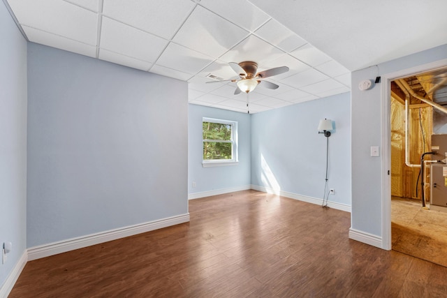 empty room featuring a ceiling fan, a paneled ceiling, baseboards, and wood finished floors