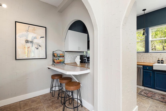 kitchen with baseboards, a breakfast bar area, blue cabinets, hanging light fixtures, and backsplash