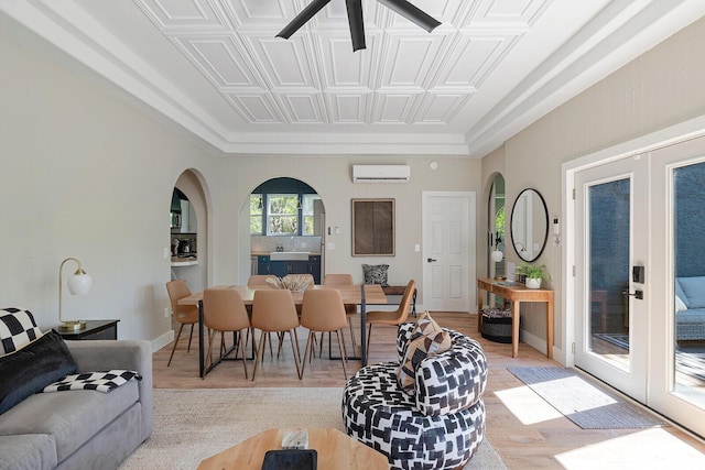 dining room featuring arched walkways, baseboards, a wall unit AC, light wood-style flooring, and french doors