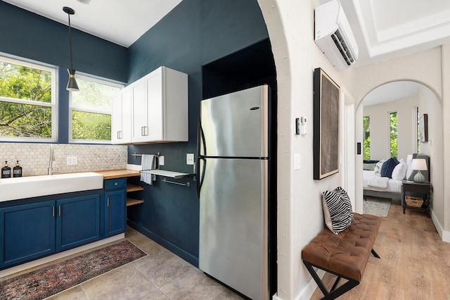 kitchen featuring arched walkways, a wall mounted air conditioner, blue cabinets, freestanding refrigerator, and a sink