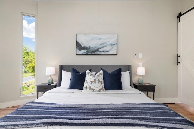 bedroom with a barn door, baseboards, and wood finished floors