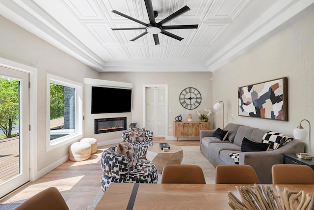 living room featuring a ceiling fan, a glass covered fireplace, an ornate ceiling, and light wood-style floors