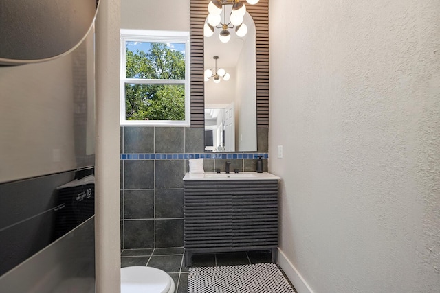 bathroom featuring a textured wall, tile patterned flooring, toilet, vanity, and an inviting chandelier