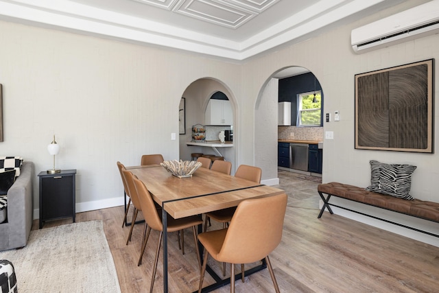 dining space featuring arched walkways, light wood finished floors, a wall mounted AC, and baseboards