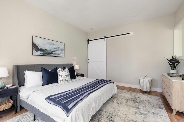 bedroom with a barn door, baseboards, and wood finished floors