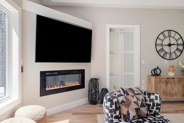 interior space with a glass covered fireplace, baseboards, and light wood finished floors