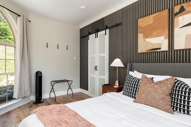 bedroom with a barn door, wood finished floors, and baseboards