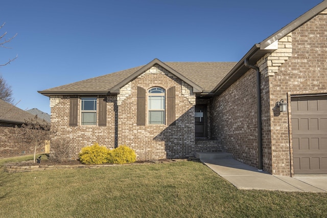 view of front of property with brick siding, an attached garage, a front lawn, and roof with shingles