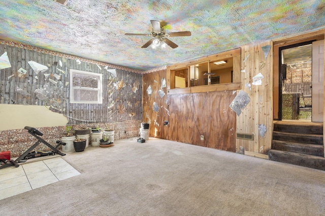 empty room featuring carpet floors, wooden walls, ceiling fan, and stairs