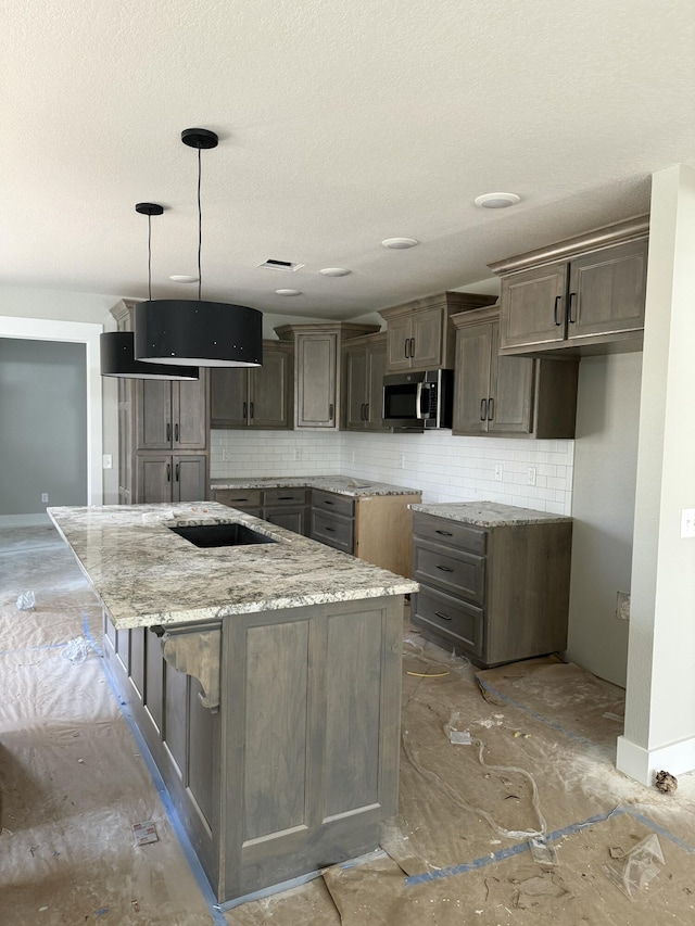 kitchen featuring light stone counters, a center island, pendant lighting, tasteful backsplash, and stainless steel microwave