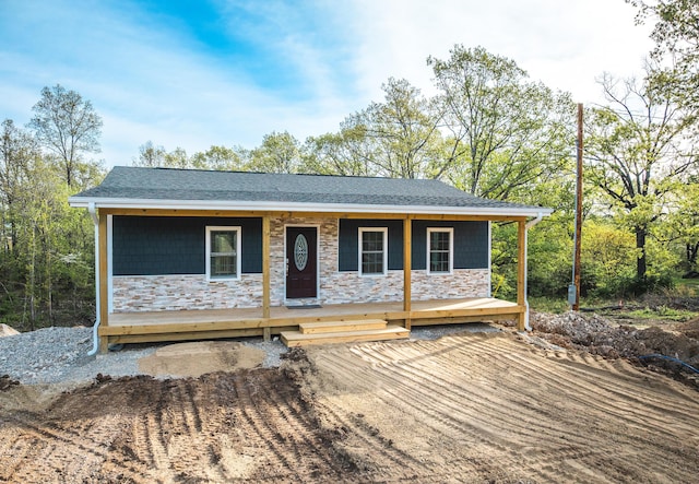 ranch-style home with a porch, a shingled roof, and stone siding