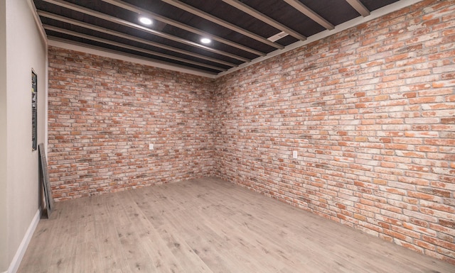 empty room featuring baseboards, wood finished floors, and brick wall