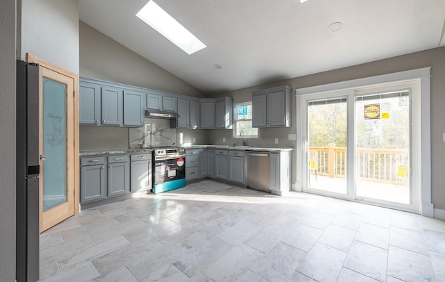 kitchen with vaulted ceiling with skylight, appliances with stainless steel finishes, under cabinet range hood, a sink, and gray cabinetry