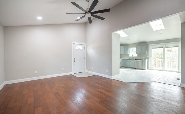unfurnished living room with a skylight, hardwood / wood-style floors, high vaulted ceiling, and baseboards