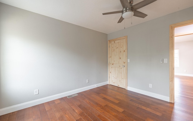 empty room with ceiling fan, visible vents, dark wood finished floors, and baseboards