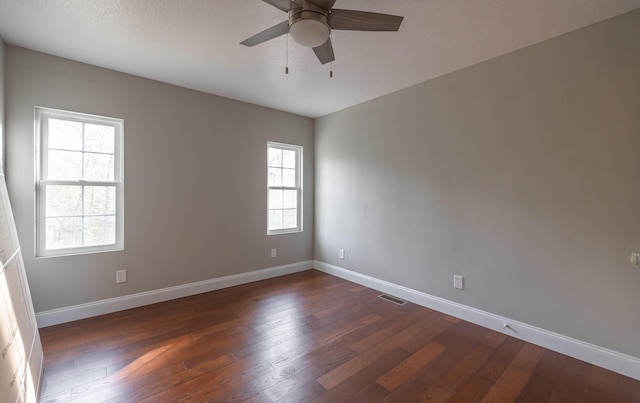 unfurnished room featuring dark wood-type flooring, visible vents, a ceiling fan, and baseboards