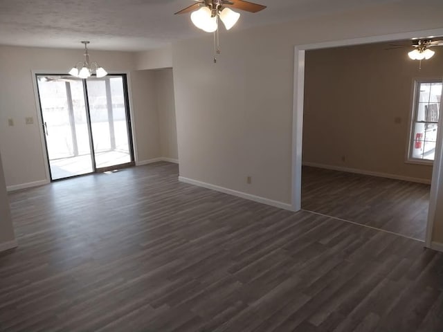 spare room with dark wood-style floors, baseboards, and ceiling fan with notable chandelier