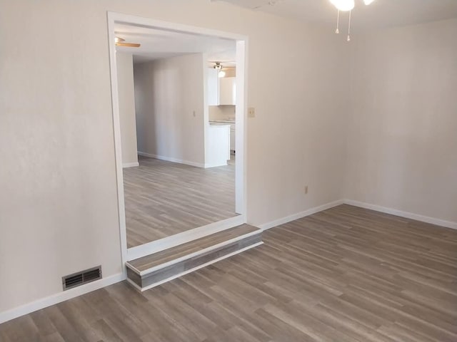 empty room with ceiling fan, wood finished floors, visible vents, and baseboards