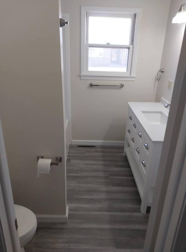 bathroom with toilet, vanity, baseboards, and wood finished floors