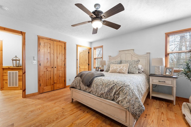 bedroom featuring visible vents, a textured ceiling, baseboards, and wood finished floors