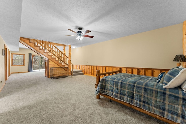 carpeted bedroom with ceiling fan, wooden walls, a textured ceiling, and wainscoting