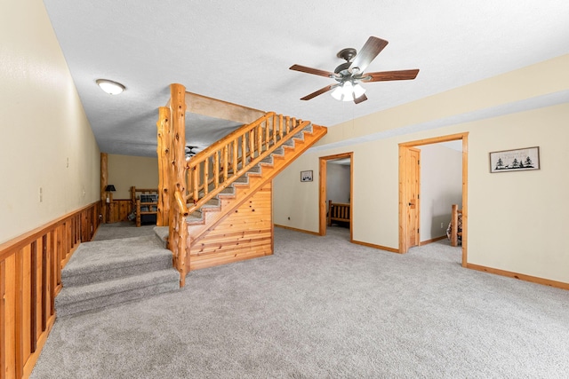 below grade area featuring a textured ceiling, ceiling fan, stairway, wainscoting, and carpet